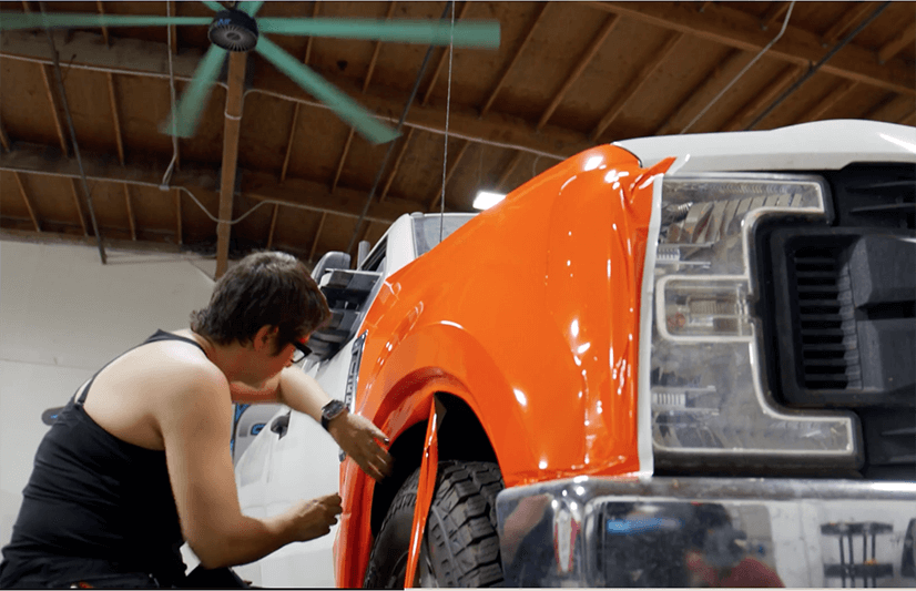 Man installing orange vehicle wrap vinyl on a truck.